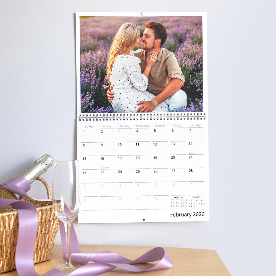 Wall calendar displaying a full-page photo of a couple embracing in a lavender field, shown above the February 2026 date grid, with spiral binding