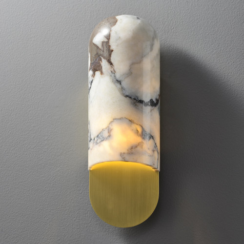 Front view of an illuminated Marble Capsule Wall Sconce Gold wall light, showing the capsule-shaped marble shade on top and the curved brass base below, with light spilling from the bottom.