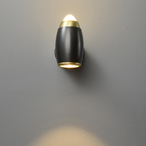 Front view of an illuminated Peas Adjustable Wall Spotlight wall light, with light coming from both ends of the oval-shaped head, featuring brass-colored ring details.