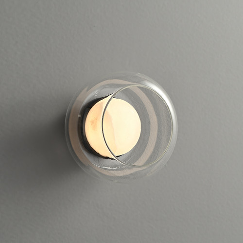 An illuminated Ava Layered Alabaster Glass Sconce mounted on a wall, viewed from the side/top angle showing the clear glass orb encasing the glowing alabaster core.
