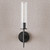 Front view of an unlit Aicken Sconce Bronze wall light, emphasizing the clear cylindrical glass shade with visible bulb inside and the metal base and arm with a brushed bronze finish.