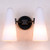 Front view of an illuminated Bianco Double Sconce Bronze double wall light, showing two glowing milky white conical glass shades and the metal base and arms with a brushed bronze finish.