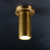 An illuminated Cameron Flushmount Brass light, angled downwards showing the cylindrical head with a burnished brass finish and light emitting from it.