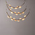 An illuminated Crescent Moon Brass Pendant Light, showing multiple tiers of brass crescent frames with translucent orb lights (alabaster material) arranged along them, emitting a soft glow.