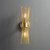 Front view of an illuminated Double Starburst Sconce Natural Brass wall light, showing the metal starburst structure radiating upwards and downwards from the center, with light bulbs visible in the middle.