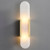 An illuminated Faith Elongated Alabaster Sconce wall light, showing the slender alabaster panel with soft light emanating from it, held by metal fixings on the sides.