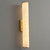 The Alabaster Cylinder Wall Light Brass mounted on a wall, with its brushed metal backplate visible, highlighting the unique veining and soft glow of the alabaster shade.
