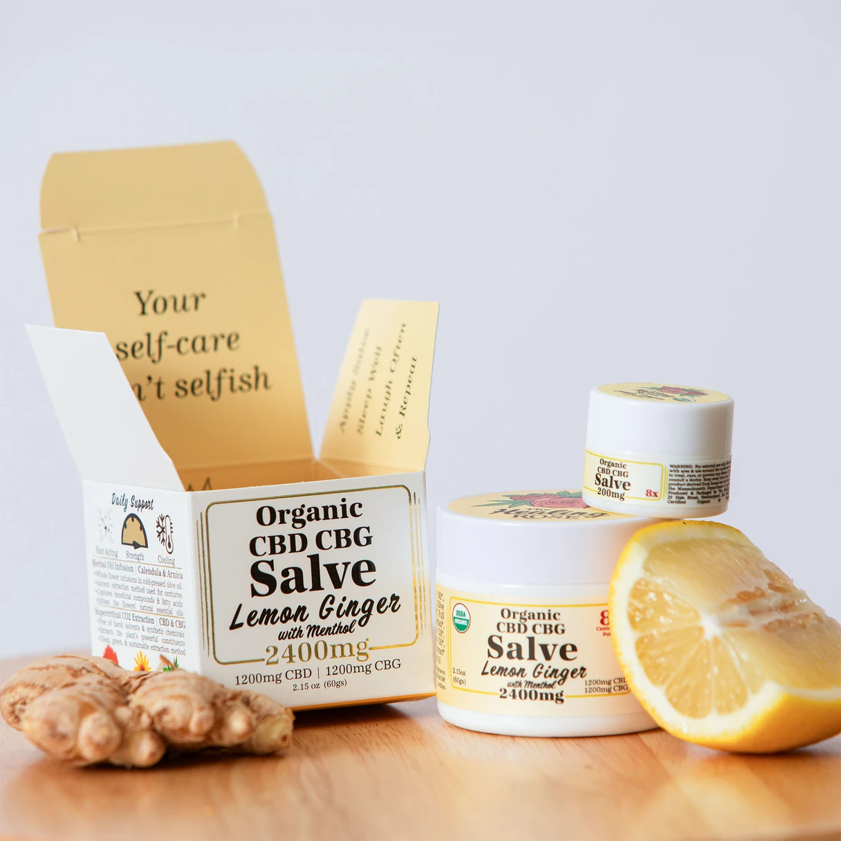 The Healing Rose Organic CBD CBG Lemon Ginger Salve with Menthol in large and small jars beside a lemon wedge and fresh ginger root