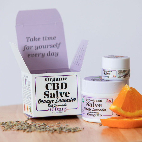 The Healing Rose Orange Lavender Organic CBD CBG Salve in large and small jars beside an orange slice and fresh lavender sprigs