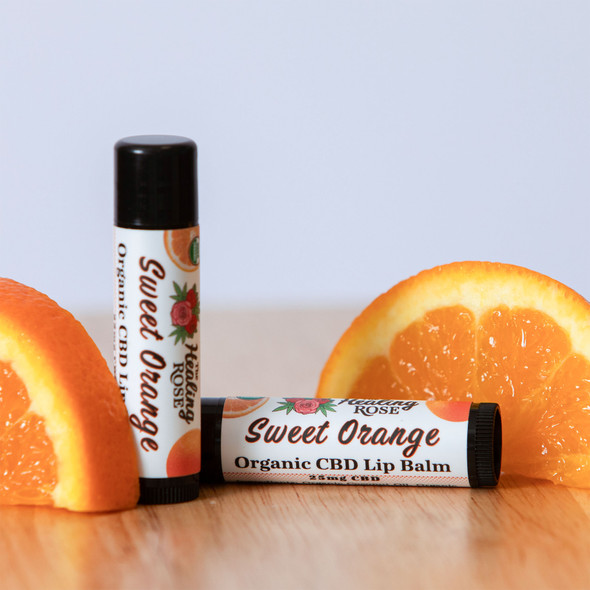 The Healing Rose Sweet Orange Organic CBD Lip Balm tubes beside fresh orange slices