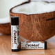 The Healing Rose Coconut Organic CBD Lip Balm tubes beside a halved coconut on a wooden surface