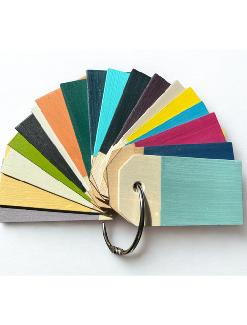A fan of rectangular wooden paint swatches in various colors—greens, teal, turquoise, orange, yellow, pink, navy, cream, and black—attached with a metal ring. The swatches are arranged in a semicircle and displayed against a white background.
