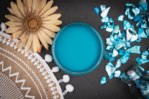 Dixie Belle Paint Peacock Chalk Mineral Paint is the perfect paint for any DIY project! Top view of open blue chalk mineral paint. Staged next to flowers and blue glass.