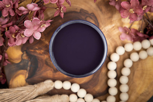 Dixie Belle Paint Aubergine Chalk Mineral Paint is the perfect paint for any DIY project! Image shows an open container of Aubergine Chalk Mineral Paint on top of a wooden stump with beads and flowers.