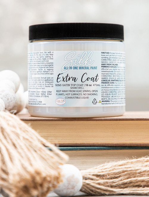 16 oz. jar of Extra Coat placed on top of 2 books with wooden beads with yarn on the ends placed next to the jar and books.