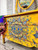 Belles and Whistles Retro Peacock - Rub On Furniture Transfer, Best Transfers for Furniture. A close up of the front drawers of a yellow dresser showing the peacock transfer on the front staged with a blanket draped on the left side.