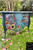 Belles and Whistles Whimsical Wonderland - Rub On Furniture Transfer, Best Transfers for Furniture.  A two drawer dresser that is chalk painted blue.  The top o the dresser is multicolored blue, yellow and teal.    The dresser sits on green grass with pink and brown flower petals scattered on the round.  Palm trees are in the background.