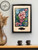 Blooming Parchment decoupage paper in a black frame hung on the wall. Staged with two black mugs on the dresser below.