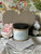 Beige painted wooden heart with a jar of Badlands in front of it. Staged on crocheted lace with faux flowers around it.