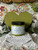 Green painted wooden heart with a jar of Everglades in front of it. Staged on crocheted lace with faux flowers and greenery.