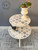 A small two-tiered table with a blue and white patterned transfer, holding a potted orchid on the top tier and a decorative bird on the lower tier, stands on a gray checkered carpet. Text reads “5anddime.ca”.