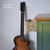 Green and blue painted furniture piece with a medium natural wood top. The drawer is pulled out and is a light natural wood with the Filigree Silkscreen Stencil applied on the side in dark gray. Staged next to a guitar leaning on the wall.