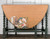 A vintage wooden table with turned green legs features a drop-leaf design. The tabletop displays a floral design with various flowers and leaves. The background has white paneled walls with "Gracie's House Painted Furniture" written above.