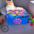 A fluffy, orange and white cat lounges on a gray surface in front of a brightly colored, painted box. The box has a vibrant cat face on the lid and a pink paw print with the number 4 on the front. Several colorful pom-pom toys are scattered next to it.