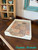 A decorative white tray with a tile-patterned decoupage paper sits on a wooden surface near a shelf with vintage items and a framed mirror. The words "Creative Moments" appear in turquoise text at the bottom right.