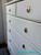 A white dresser with gold ring pull handles and subtle gold trim, featuring multiple drawers. The words "Creative Moments" appear in turquoise script in the bottom right corner.