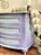 Dixie Belle Paint Lucky Lavender Chalk Mineral Paint is the perfect paint for any DIY project!
Short dresser painted in Lucky Lavender Chalk Mineral Paint  with hints of baby blue in front of drawers and around piece. Staged with white flowers around the piece.