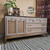 A vintage-style sideboard with rattan paneling, brass handles, and a wood top sits against a tan wall. A plant, decor items, and a watermark reading "Retro Revival" are on and above the sideboard. A patterned rug is on the floor.