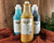 Image of Yellow, Green, and Blue 32 oz. Patina Spray Refills. Staged on an orange blanket with faux greenery and faux wood behind it.