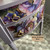 A close-up of a painted dresser with floral designs and gold gilded handles. An arrow points to a handle and key hole, labeled "Gold Gilding Wax." The text "The Top Drawer RVA" is in the lower right corner.