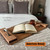 A cozy bedroom scene with an open book on a wooden tray positioned on a textured bedspread. A lit candle and a cork coaster are also on the tray. A bed with tufted pillows is in the background. Text reads "American Honey."