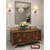 Wooden dresser with floral arrangement in a room with a large mirror and wall lights.
