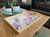 Whitecap Silk All-In-One paint is perfect for painting kitchen cabinets, bathroom cabinets and painting furniture.  A wooden serving tray that is chalk painted white on the inside and has the Translucent Garden Transfer applied to it sits on a brown wooden table.  A teal circular tray sits on the table behind the tray with several white pots holding aloe plants.  Behind the table is a fireplace in a brick wall and a black pot.