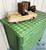 Belles and Whistles Harlequin - Stencil provides an extra decorative touch to any project!
This is a picture of a green side table with two drawers. The pulls are metal and painted in a lighter green color.  There are two pulls per drawer.  The top and sides of the table is stenciled in a Harlequin design  The colors are two different shades of green.  One is the orginal color of the side table and the other a very pale greenish-white; the same as the drawer pulls.  It is staged with a large, model, old-style, 1950's, convertible that is painted in beige and the interior is dark brown.  There are 6 books on the top.  4 brown books and 2 blue.  Holding the books up so they don't fall off the table is a 1950's camera case which is brown leather.  The wall behind the side table looks like a lot of crown molding next to each other.  The molding is placed lengthwise.  The floor that the table rests on is baby blue.