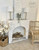 WoodUBend Trim #TR715 (Set of 2).  A white chalk painted fireplace with several different WoodUBend embellishments placed in the corners and along the top of the arched opening.  Several brown logs sit inside of the fireplace.  Staged on tan carpet in front of a white wall, with a brown burlap basket holding white flowers to the left and a brown wicker chair to the right.  Two silver lamps with white shades and a vase with eucalyptus sit on top.  Also a white chalk painted sign with black cursive writing sits behind the vase.