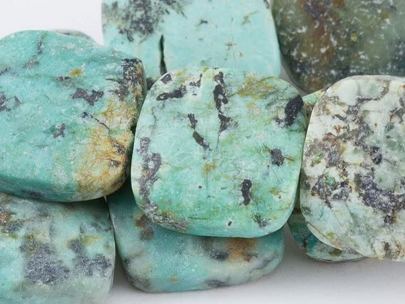 Modern style comes alive in the Dakota Stones 12mm matte African Turquoise Jasper square beads. Available by the strand, these gemstone beads feature a square shape with rounded corners. You can use them in necklaces, bracelets and even earrings. They feature deep turquoise color with a black matrix. The matte finish adds an organic style. This stone is mined in Africa and is actually a type of spotted teal Jasper rather than turquoise. It is given its industry name because the matrix structure and shade is similar to that of turquoise. It has a Mohs hardness of 6. Metaphysical Properties: Often called the stone of evolution, African Turquoise Jasper encourages growth and development not only in the body, but in the mind. Some spiritualists believe that it will attract money to the wearer.Because gemstones are natural materials, appearances may vary from piece to piece. Each strand includes approximately 16 beads.