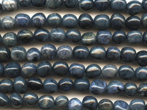 Your designs will stand out with daring color when you use the dumortierite 8x10mm tumble nugget beads from Dakota Stones. These beads feature a nugget shape that makes each bead look like a pebble. All of the beads display a dark blue color streaked with hints of black. Dumortierite is a fibrous variably colored aluminum boro-silicate mineral. They crystals are vitreous and vary in color. Metaphysical Properties: Known as the "Stone of Order," dumortierite is said to help boost intellectual perception and to help in becoming more organized.Because gemstones are natural materials, appearances may vary from piece to piece. Each strand includes approximately 14 beads.Length 10-11mm, Width 9-10.5mm