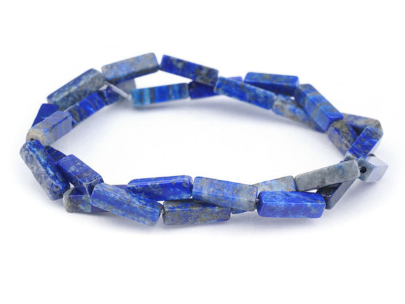 Deep blue style fills these lapis lazuli rectangle tube beads from Dakota Stones. Available by the strand, these bold beads are rectangular in shape and feature glittering golden color sprinkled over a dark blue and grey background. Lapis lazuli is a semi-precious stone that contains primarily lazurite, calcite and pyrite. It was among the first gemstones to be worn as jewelry. Showcase these stunning gemstone beads in your next design. Metaphysical Properties: Lapis lazuli is said to enhance insight, intellect and awareness. Because gemstones are natural materials, appearances may vary from bead to bead.