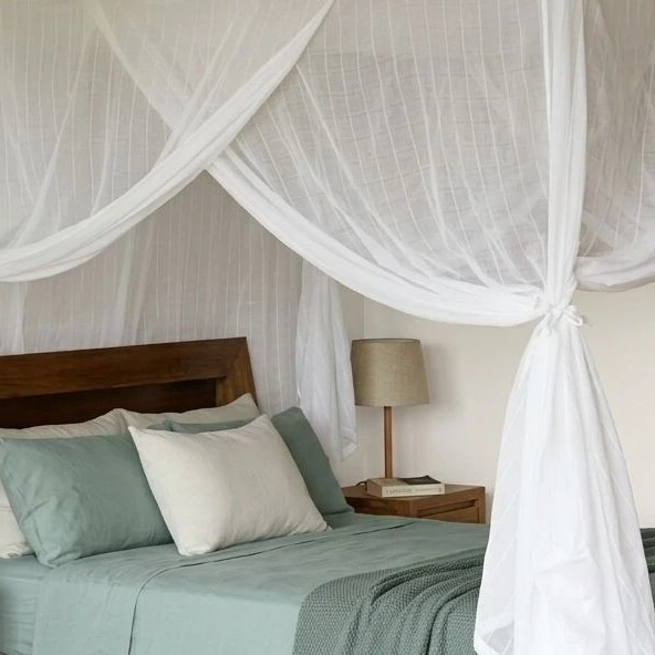 White cotton box mosquito net tied open at the corner of a bed with sage green linen and a timber headboard