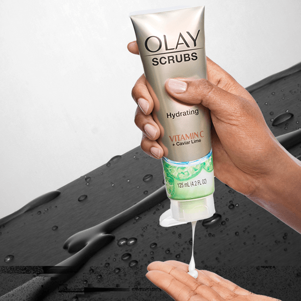 Hand squeezing bottle of Vitamin C + Caviar Lime Face Scrub floating on wet background. Promo reads: Extra $2 OFF one skin care item with code SKIN.