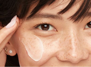 Female Asian-American model with light pink manicured nails applying moisturizer as step 3 - the last step - of her skin care routine.