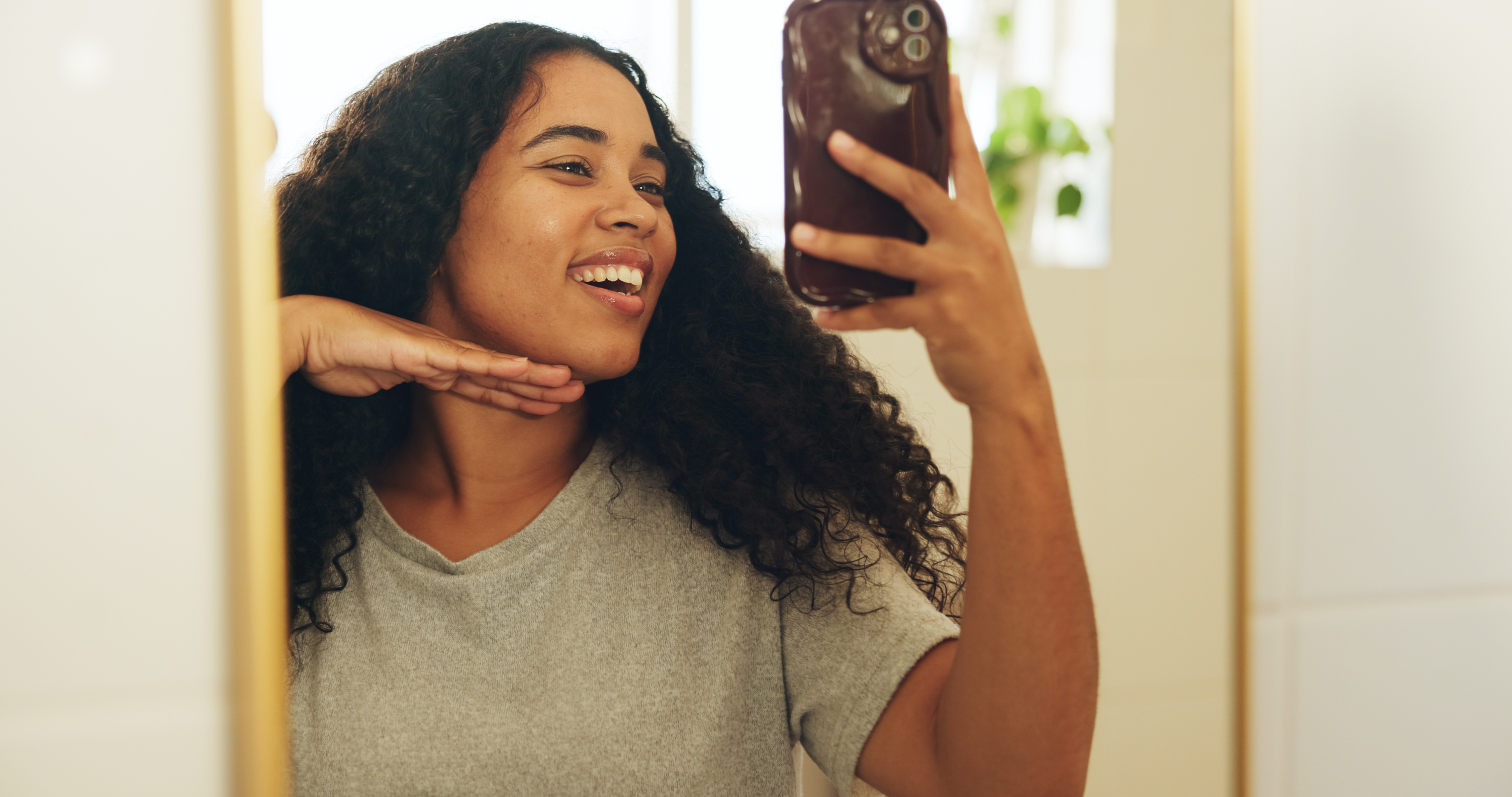 Young woman smiling and posing her face at an angle while holding up her phone to take a selfie photo.