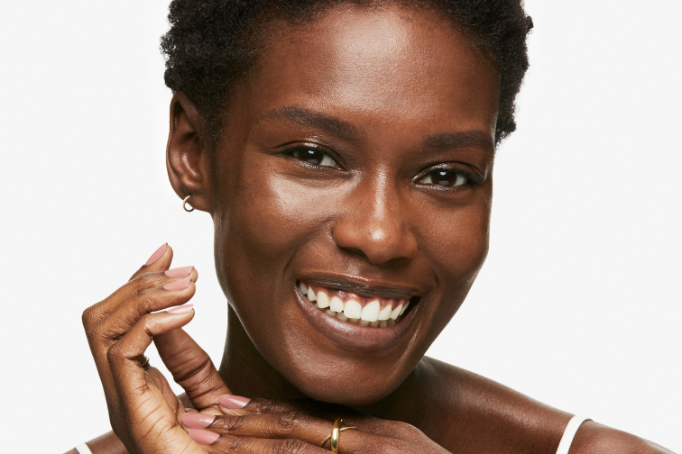 African American woman smiling with her hands clasped under her chin.