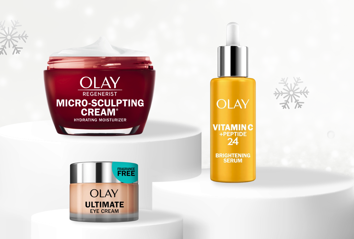 Red glass jar of Olay Micro-Sculpting Cream moisturizer on a pedistool next to Olay Vitamin Peptide 24 alongside Olay Ultimate Eye Cream with snowflakes falling behind. 