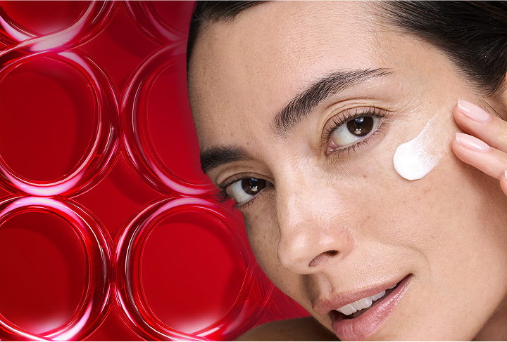 Smiling woman applying Olay Micro-Sculpting face cream moisturizer on her left cheek