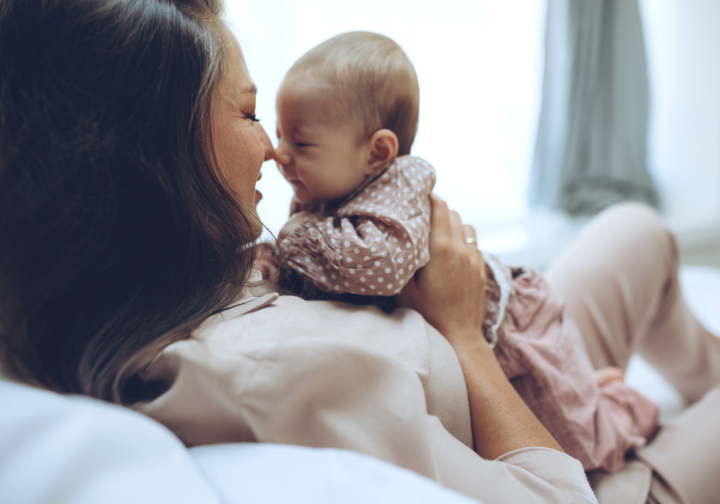 A mother laying on a sofa touching noses and holding her baby on her chest